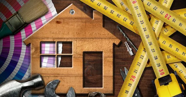 A hammer, tape measure, and other tools used for Denton home maintenance placed next to a wooden cutout of a house.