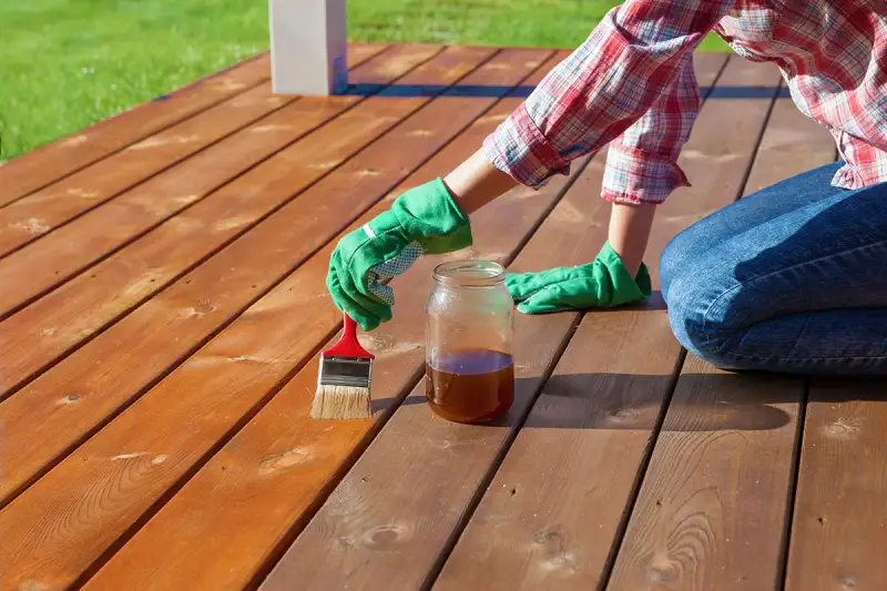 An individual weatherproofing a deck by staining it.