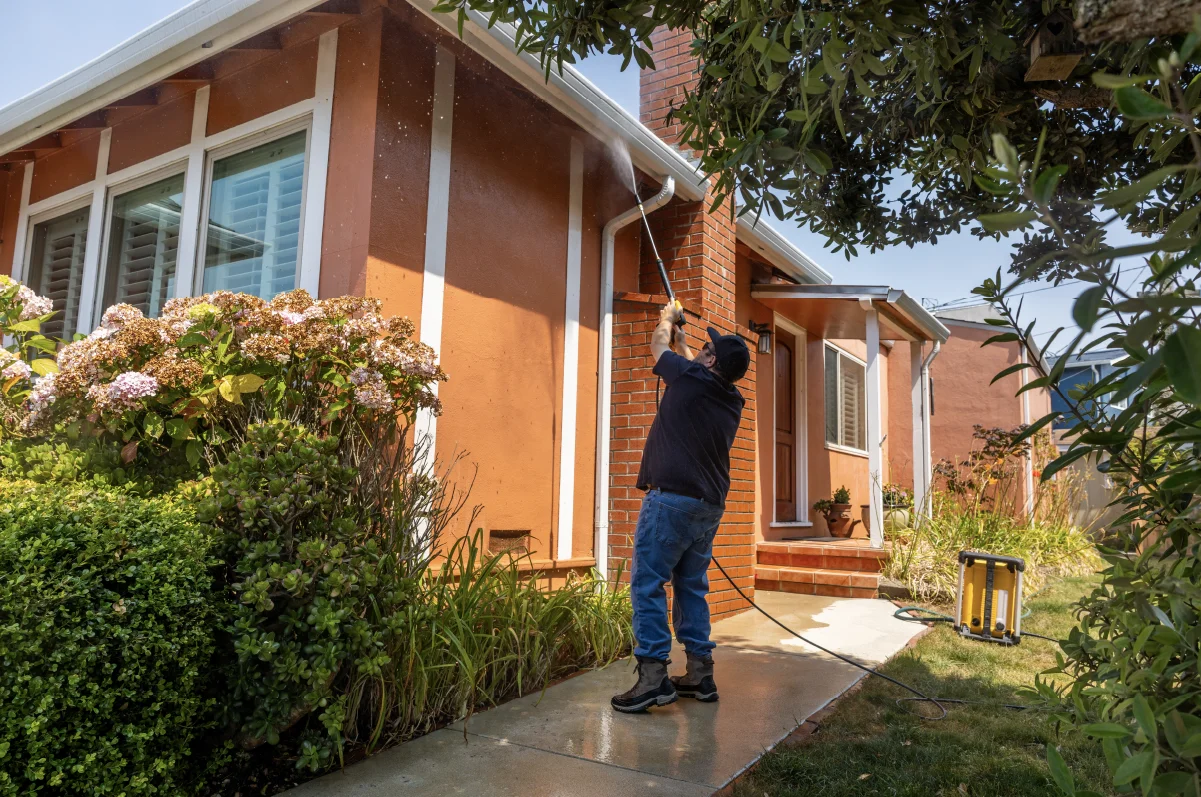 Man cleaning house gutters using a pressure washer.