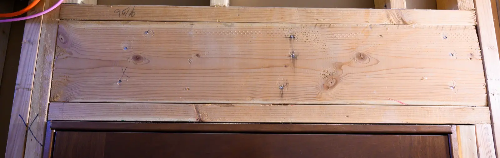 Exposed wooden wall studs with various notches and pencil markings, indicative of construction work and structural examination.