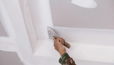 A handyman using a putty knife to spread drywall compound for professional ceiling repairs or finishing an installation.