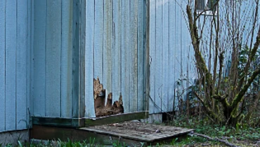 A home with old, blue siding that has been cracked and damaged at the bottom and requires siding repair services.