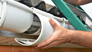 A handyman standing on a ladder as they replace a section of a gutter system while completing gutter repairs on a residential roofline.