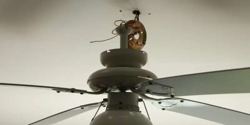 A black ceiling fan dangles off its mount with electrical wires disconnected during installation.