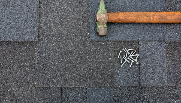 A hammer and nails lying on top of a roof after new shingles have been installed during an appointment for roof repair.