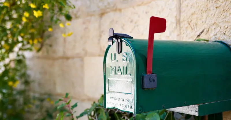 A green mailbox with a red flag placed near the exterior wall of a home after receiving mailbox repair service