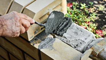 A handyman spreading fresh mortar over a section of a stone fence as he replaces a stone during an appointment for Walpole masonry repair.