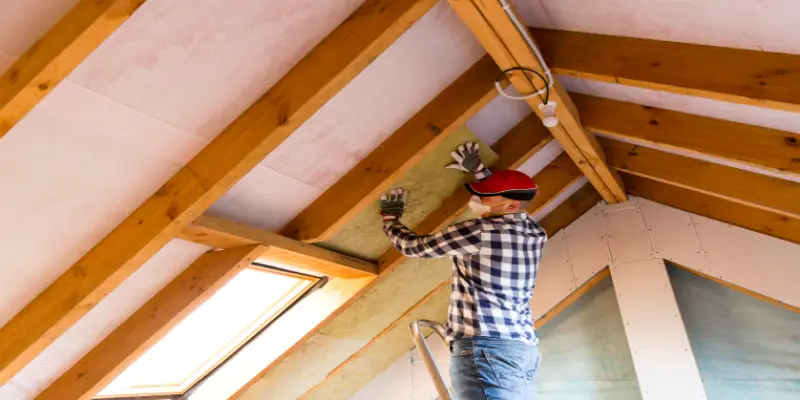 A handyman installs thermal roof insulation layer - using mineral wool panels.