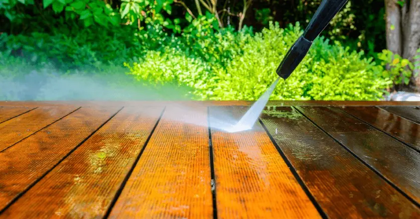  A close-up of the nozzle on a power washing machine as it’s used to clean a wooden deck by blasting it with high-pressure water.