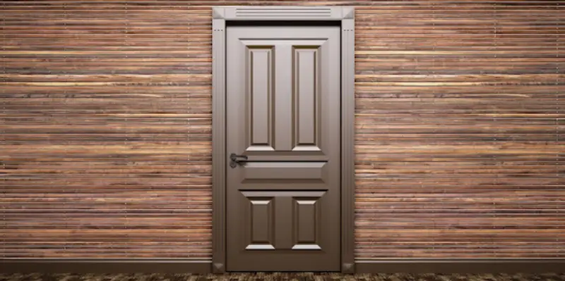 A closed brown door viewed from the interior of a residential room with walls made of thin wood strips.