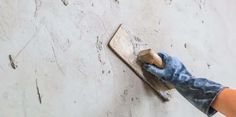 The hand of a handyman using a float to apply new stucco to the outside of a home during a Flower Mound stucco repair project.