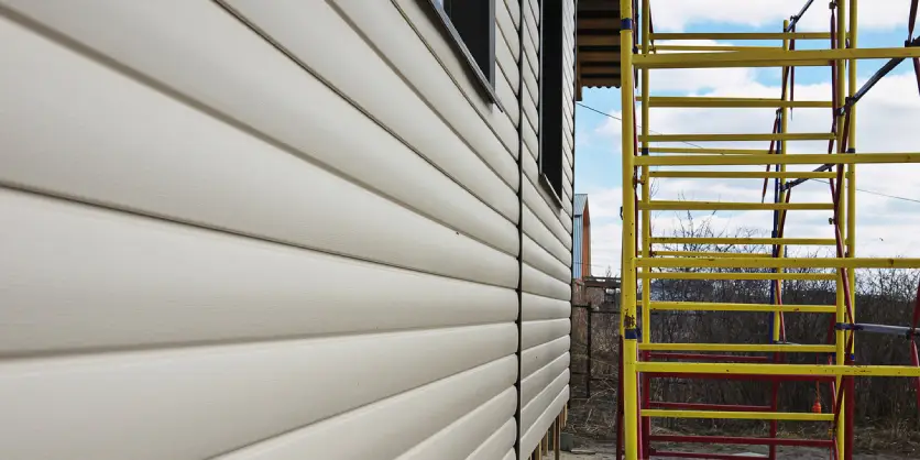 New siding on the exterior of a house, and metal scaffolding that has been set up to facilitate ongoing siding repairs.