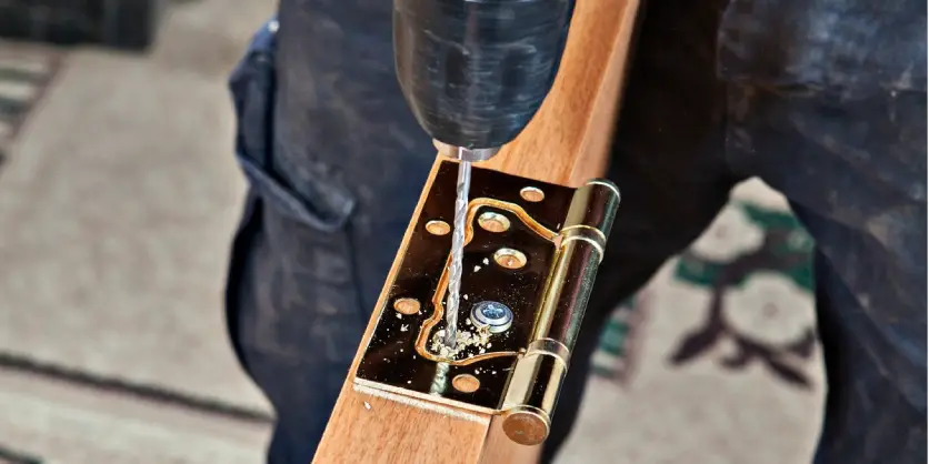 A handyman using a screwdriver to attach a hinge to a door slab while providing door installation service.