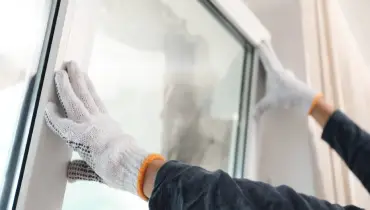 A close up of a handyman in the process of completing window installation and tilting the new window unit into place within an existing frame.