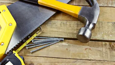 A hammer, saw, nails, and measuring tape lying on a worn deck in need of deck repair services.