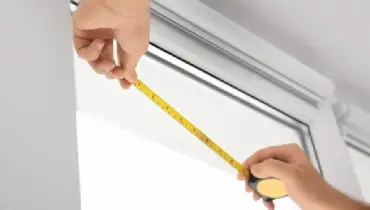 A handyman using measuring tape to measure the length of a window before starting residential window repairs.A handyman using measuring tape to measure the length of a window before starting residential window repairs.