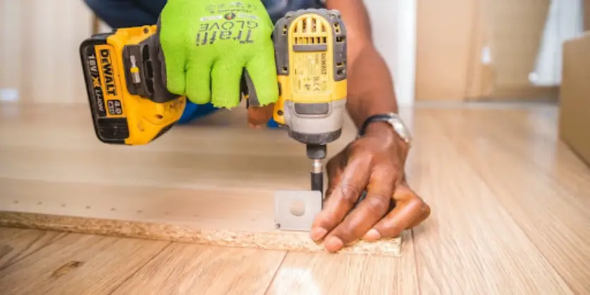 A handyman using a cordless power drill to screw on mounting brackets during an appointment for furniture assembly.