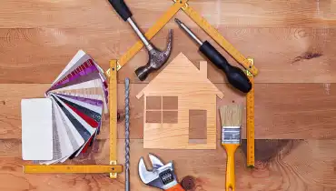 Hand tools and paint color samples arranged in the shape of a house around a house-shaped wood cutout