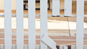 A white picket fence with broken pickets creating a hole that must be fixed with fence repair services.