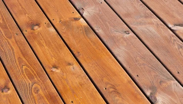 Wooden deck boards on a porch that has been partially refinished after receiving service for deck repairs.