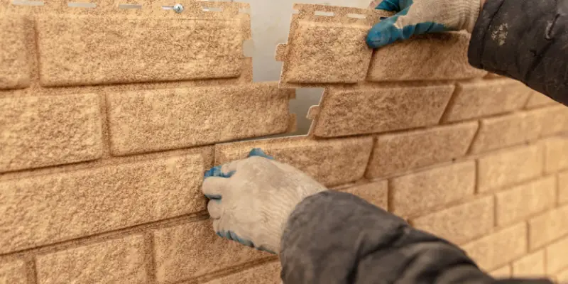 A handyman installing new sections of brick veneer siding on the outside of a house during a siding repair job.