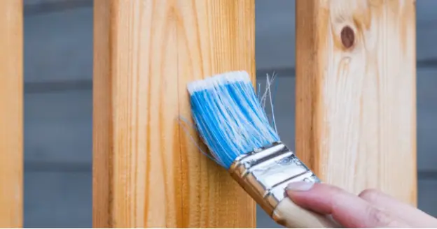 Fence slats being stained with a paint brush.