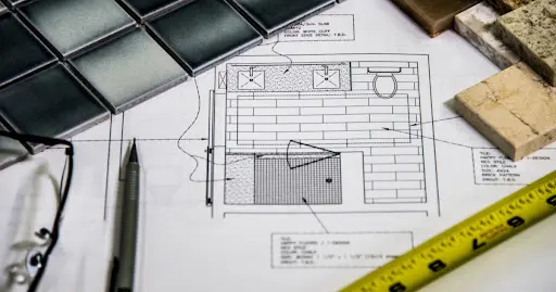 Home improvement plans surrounded by a ruler, wood, pencils and tile samples.