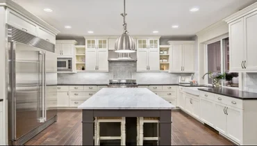 Kitchen with wood floors and white cabinets and marble counter tops.