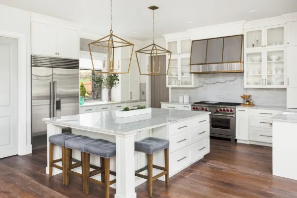 Beautiful white kitchen in luxury home. Features large island, pendant lights, and hardwood floors.