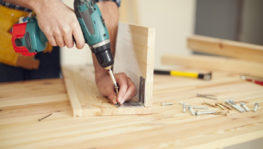 Closeup of a person holding a drill and screw into a piece of wood.