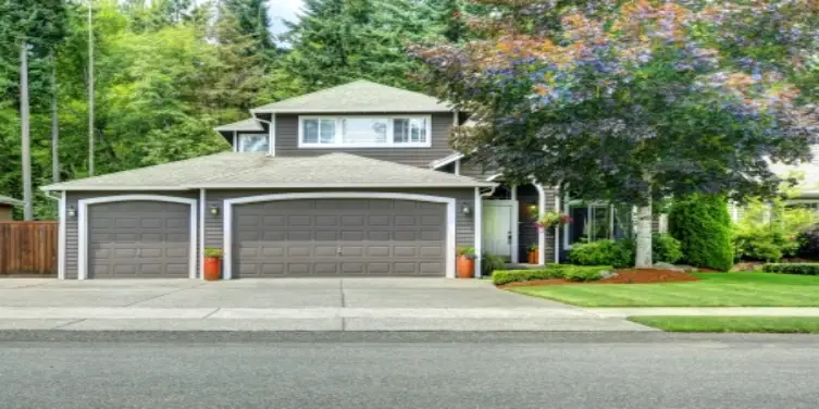 House with three car garage, with driveway, sounded by trees.