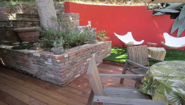 A wooden deck with chairs and a brick wall.