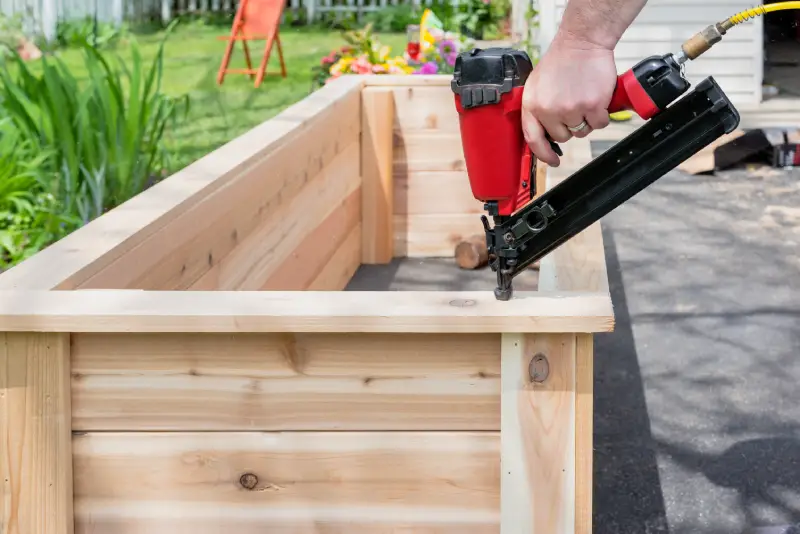 Close-up of a man using a pneumatic nail gun to build a diy raised garden bed