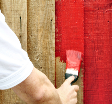 Someone painting a wooden fence red.