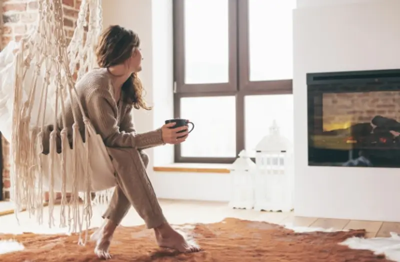 Young woman holding a coffee cup relaxing in front of an electric fireplace.