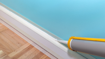 A person using a caulking gun to apply caulk to a baseboard.