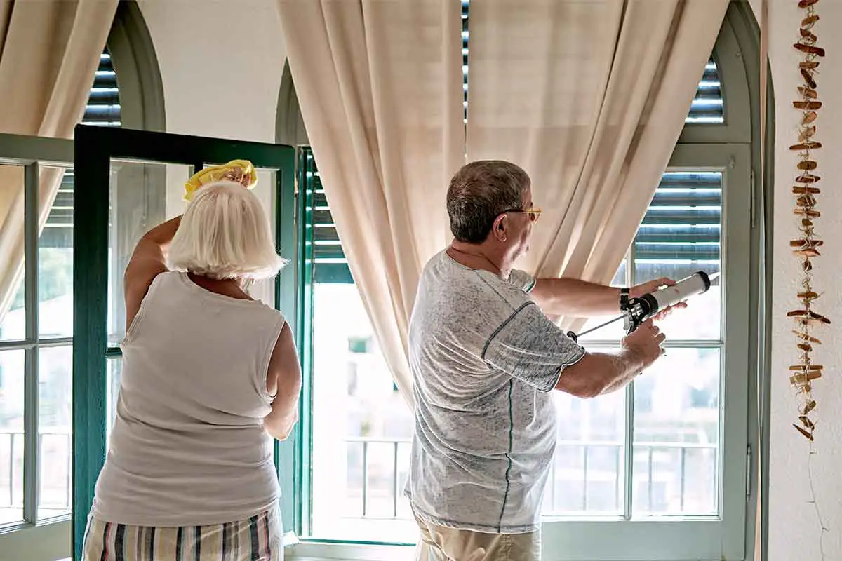 Couple adding caulk to insulate windows