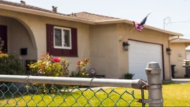 Home displaying American flag behind chain link fence.