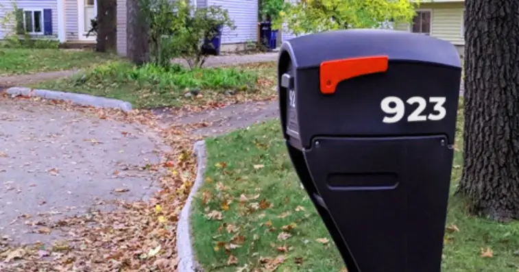 A black mailbox installed at the edge of a residential property, with red flag in the down position.