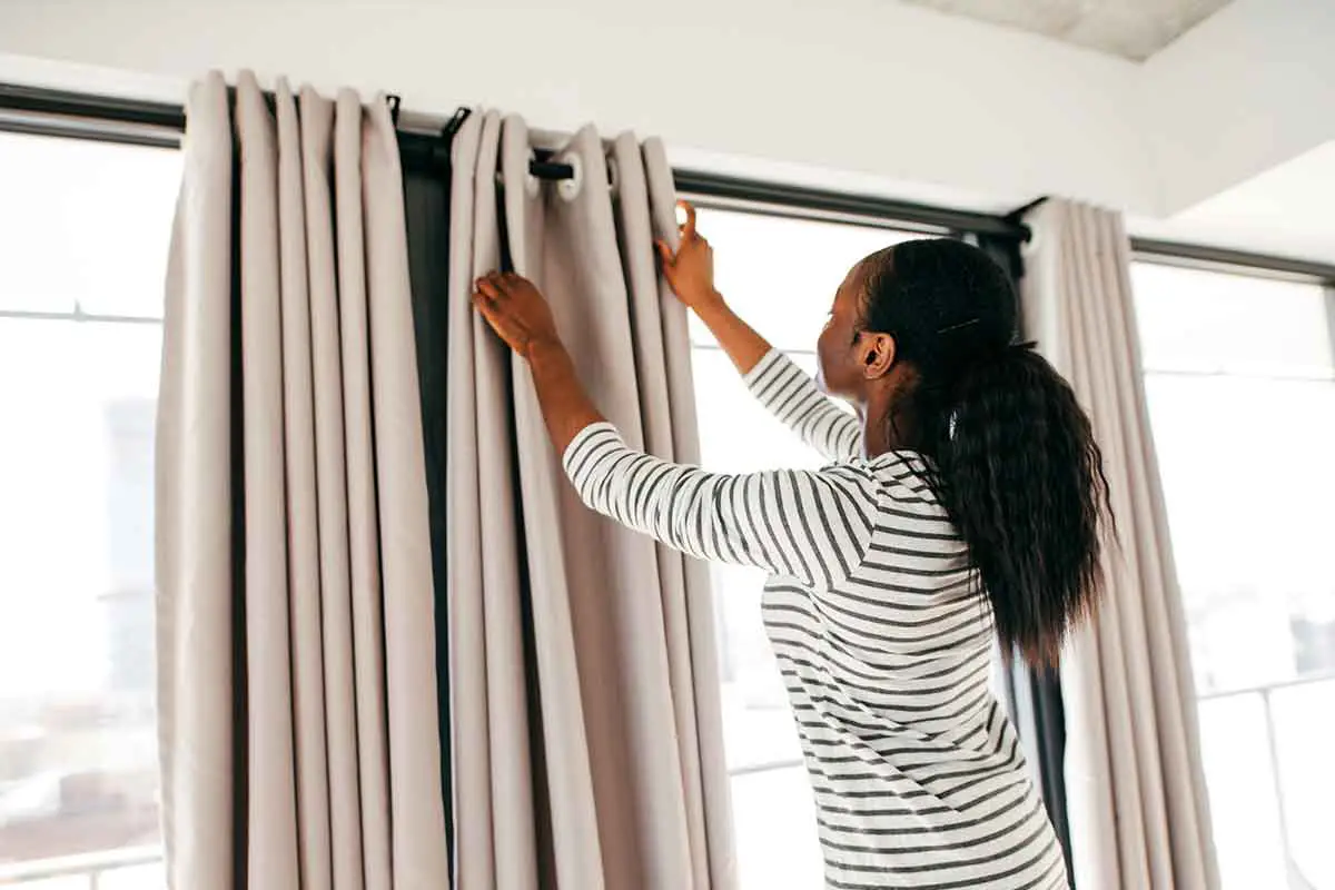 Person hanging thermal curtains in their living room to insulate the windows