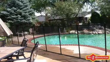 Swimming pool enclosed in fence with Mr. Handyman logo.