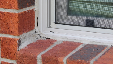 Dried worn-out caulking around exterior windowpane of brick home.