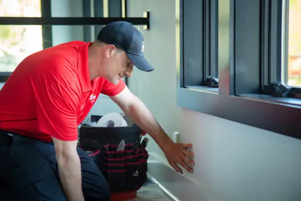 Mr. Handyman technician fixing drywall beneath a window.