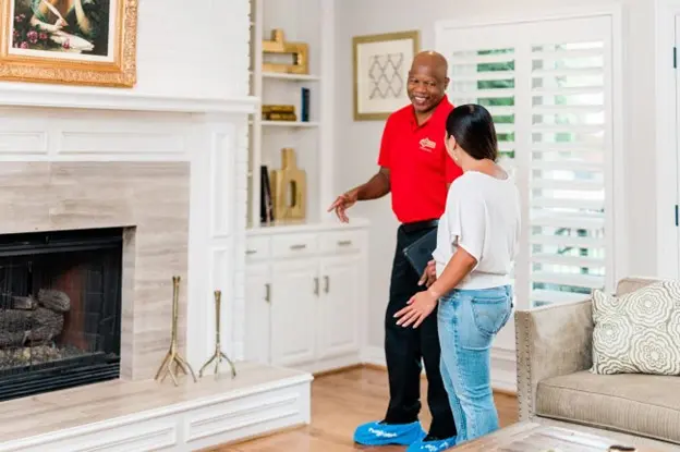 Mr. Handyman standing in a living room with a client and talking about home repairs.