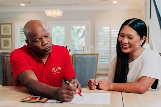 Mr. Handyman reviewing paperwork with a female client at a table.