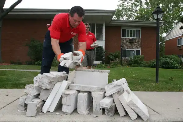 Mr. Handyman of Wheaton-Hinsdale technician piling up concrete in front of multifamily residence.