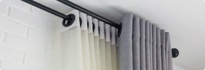 Closeup of a double curtain rod with white curtains layered behind grey blackout drapes.