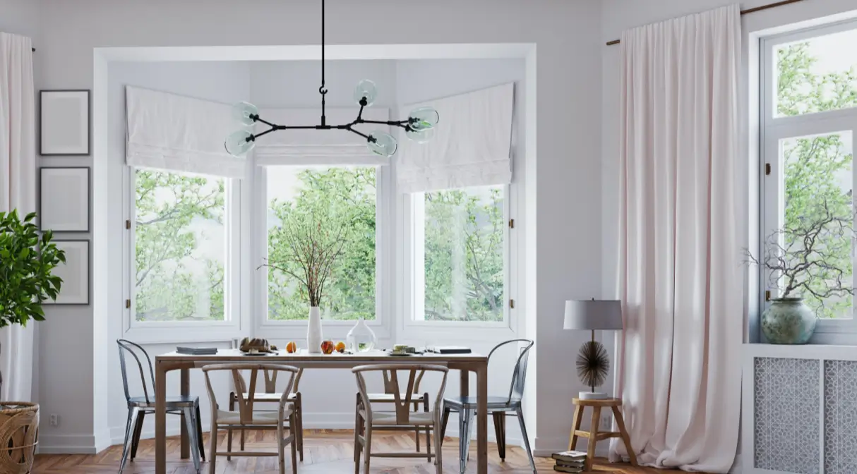 A modern dining room featuring large windows adorned with white curtains and floor-length drapes.