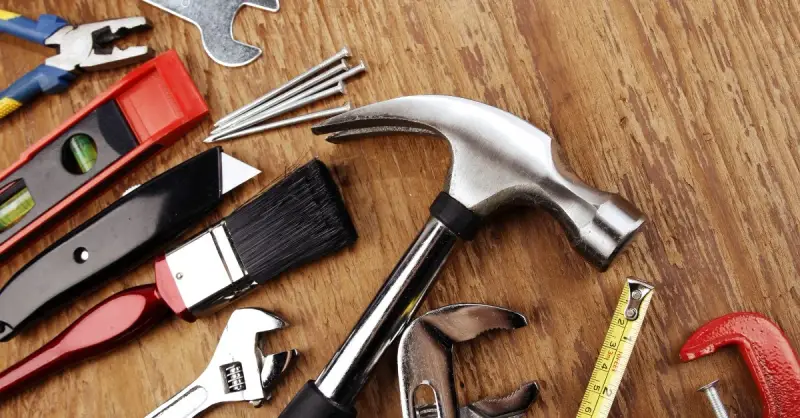 A hammer, wrench, brush, utility knife, level and other tools laid out on a wooden surface for use by a handyman in Cross Timber, TX.