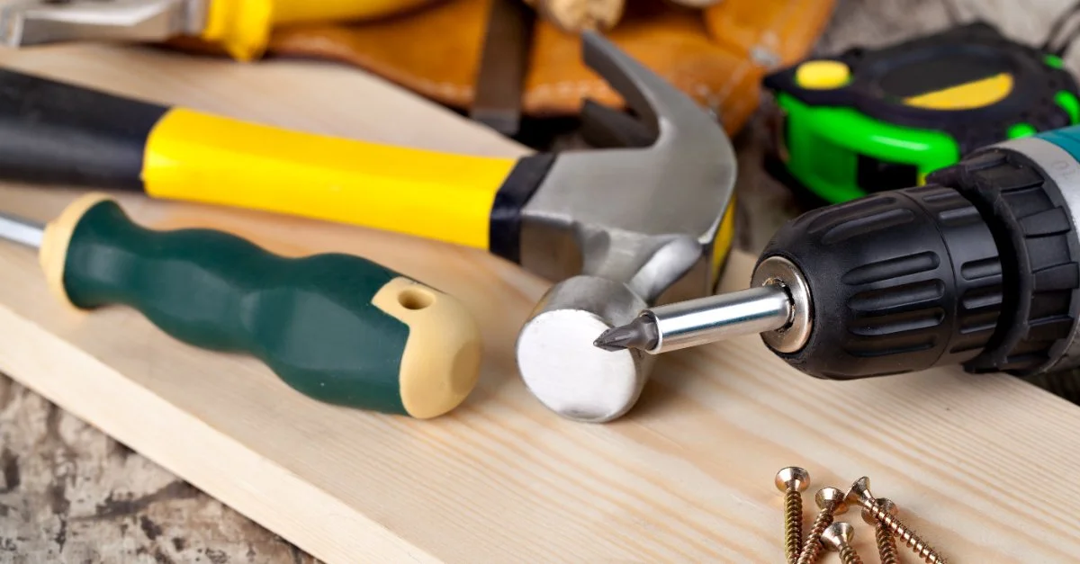 A hammer, screwdriver, power drill, and several screws resting on a wood board before being used by a handyman in Greenwich, CT.